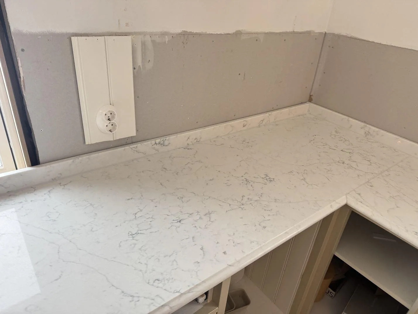 Köksbänkskiva i Technistone Mystery White i vinkel runt ett hörn med grå marmorlik ådring i ett kök under montering i Habo.