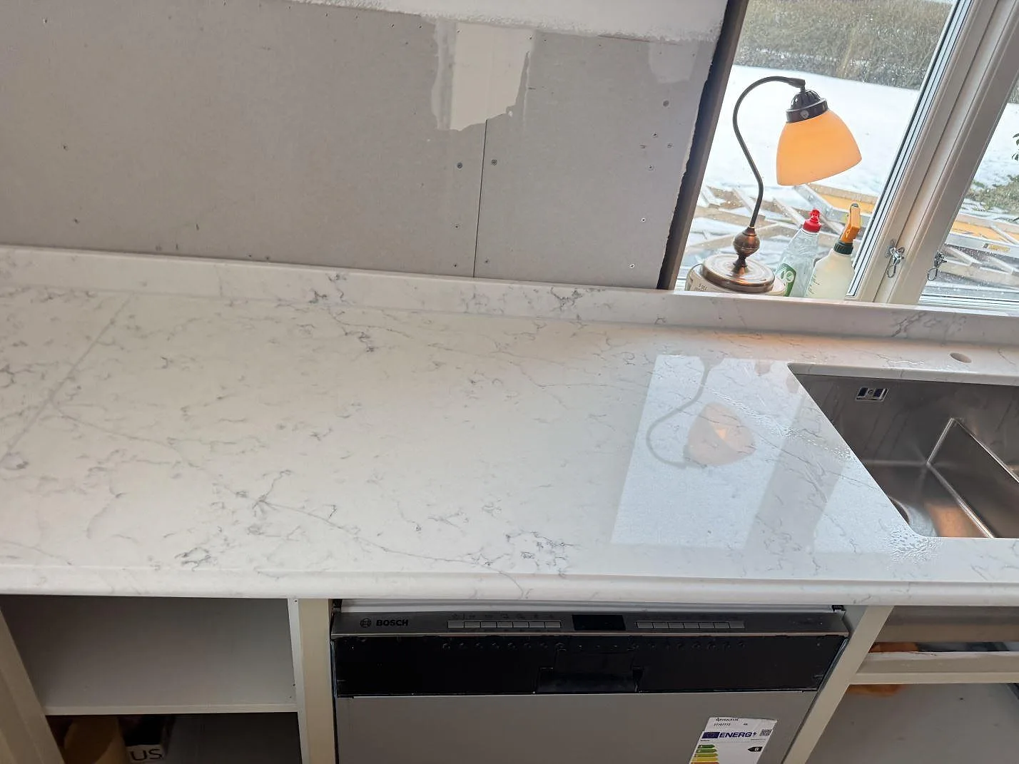 Köksbänkskiva i Technistone Mystery White med underlimmad rostfri diskho och integrerad diskmaskin i ett kök i Habo.