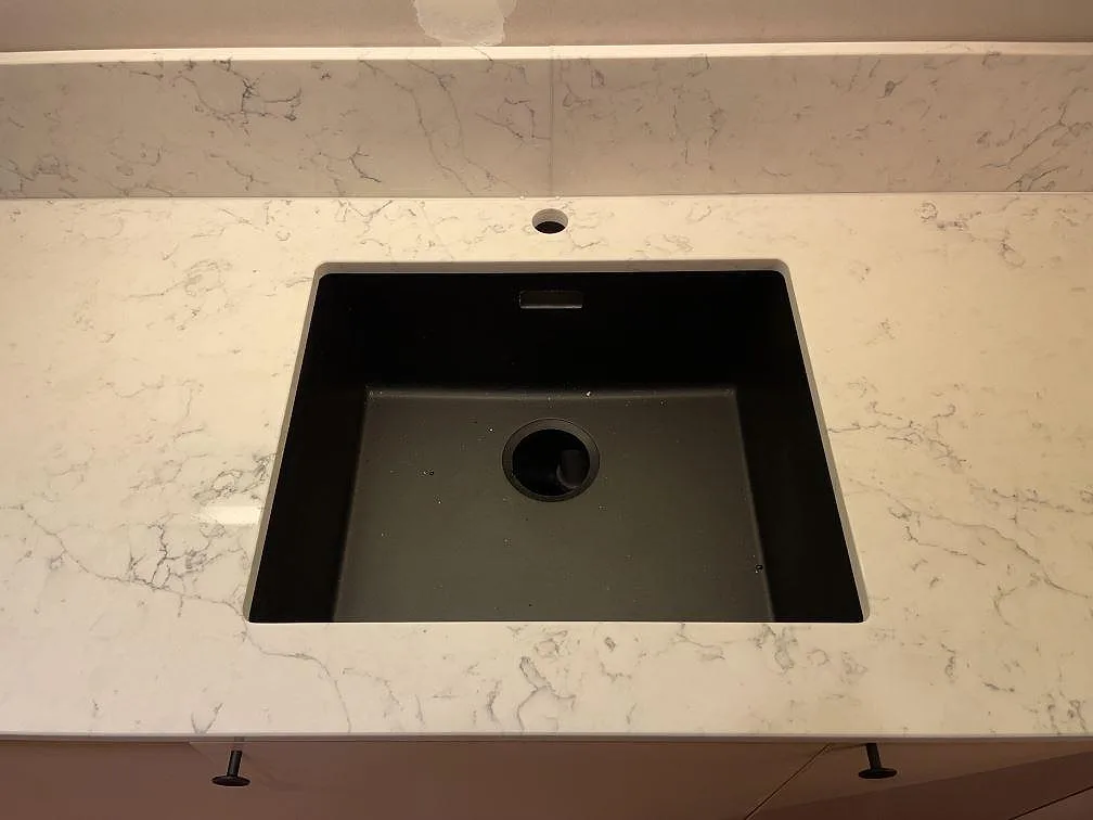 Närbild på polerad köksbänkskiva i Technistone Mystery White med mörk diskho, kranhål och stänkkant i ett kök i Hammarö.