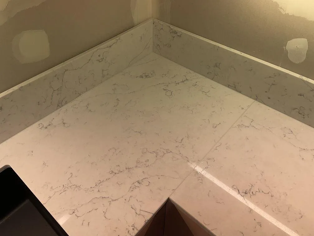 Hörnparti av köksbänkskiva i polerad Technistone Mystery White, vit kvartskomposit med tydlig grå ådring och stänkkant i Hammarö.
