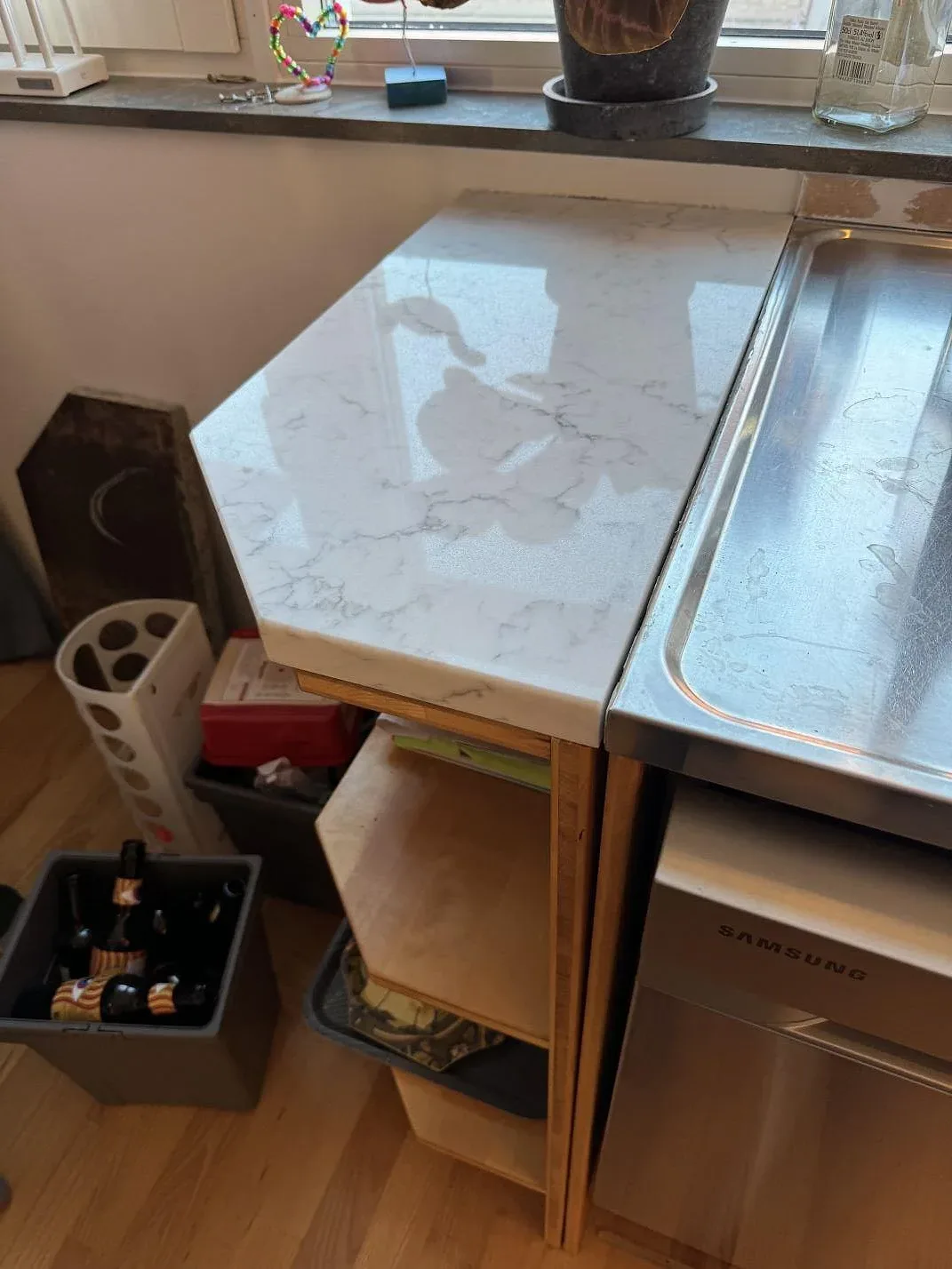 Sidovänd bild av polerad Technistone Mystery White komposit vid rostfri diskbänk och träinredning i Hjärup.