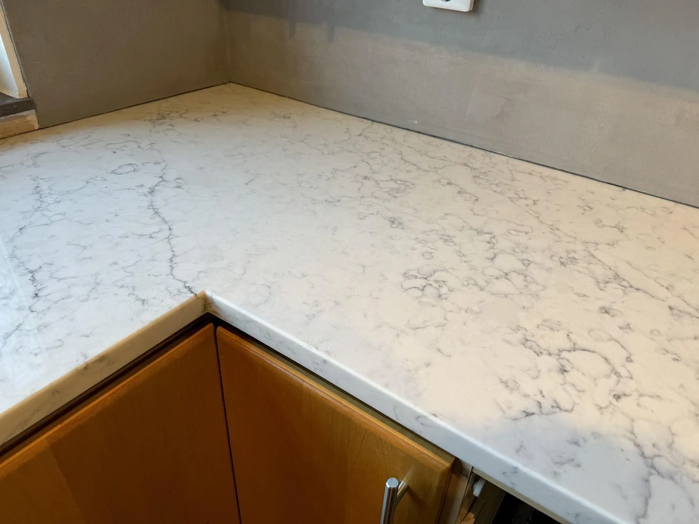Närbild på hörn i polerad Technistone Mystery White komposit med grå ådring ovanför träskåp i Hjärup.