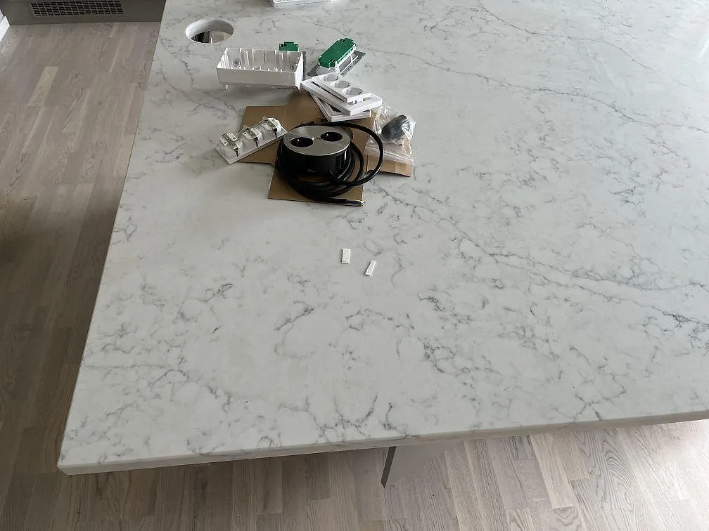 Stor köksö i polerad Technistone Mystery White med urtag för uttag under montering i ett kök i Hököpinge.