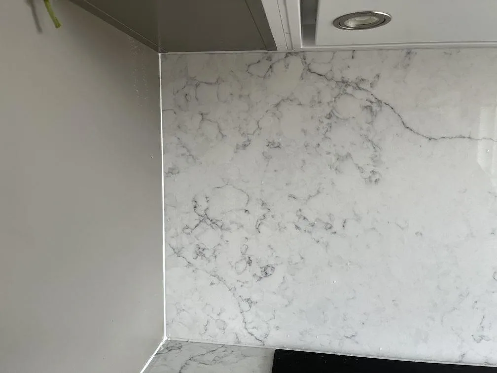 Hörnparti av stänkväggen i vit Technistone Mystery White med spotlight ovanför i ett kök i Hököpinge.