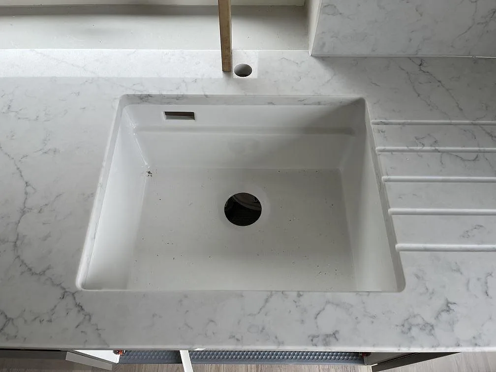 Polerad köksbänkskiva i Technistone Mystery White med underlimmad diskho och borrat hål för köksblandare i ett kök i Hököpinge.