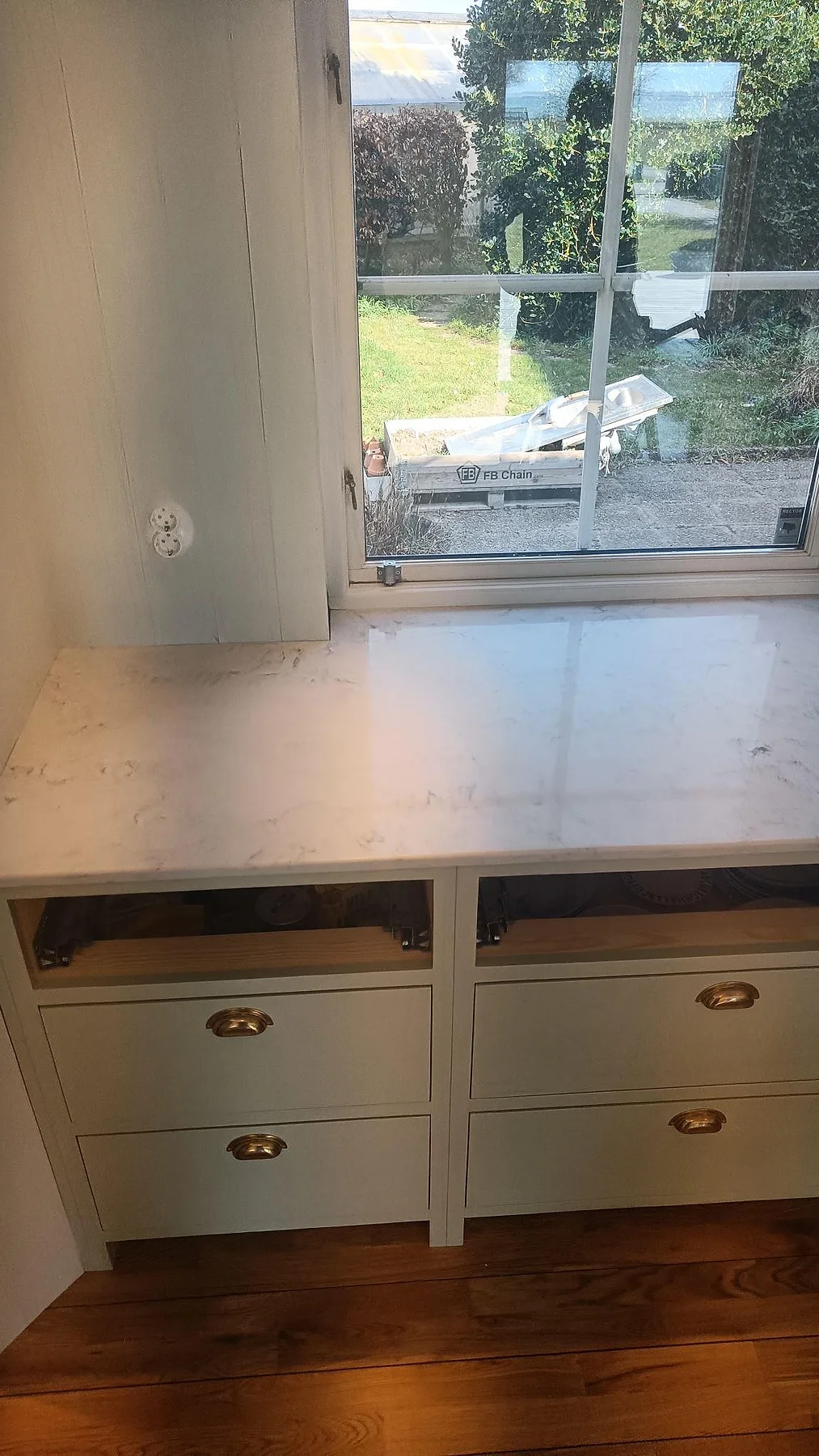 Polerad bänkskiva i vit Technistone Mystery White vid ett fönster med ljusa lådfronter och mässingsbeslag i ett kök i Höllviken.