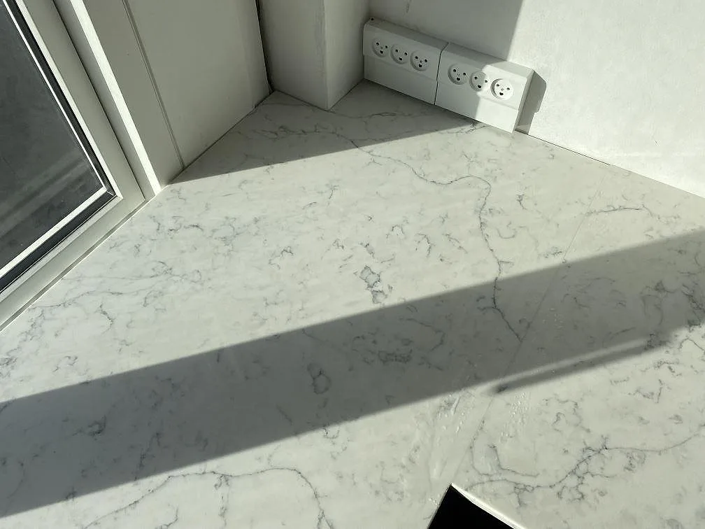 Hörndetalj av köksbänkskiva i polerad Technistone Mystery White komposit vid fönster och vägguttag i Kbh k.