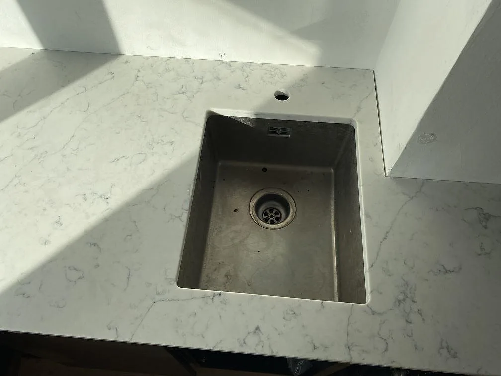 Närbild på rostfri diskho i polerad köksbänkskiva av Technistone Mystery White komposit i Kbh k.
