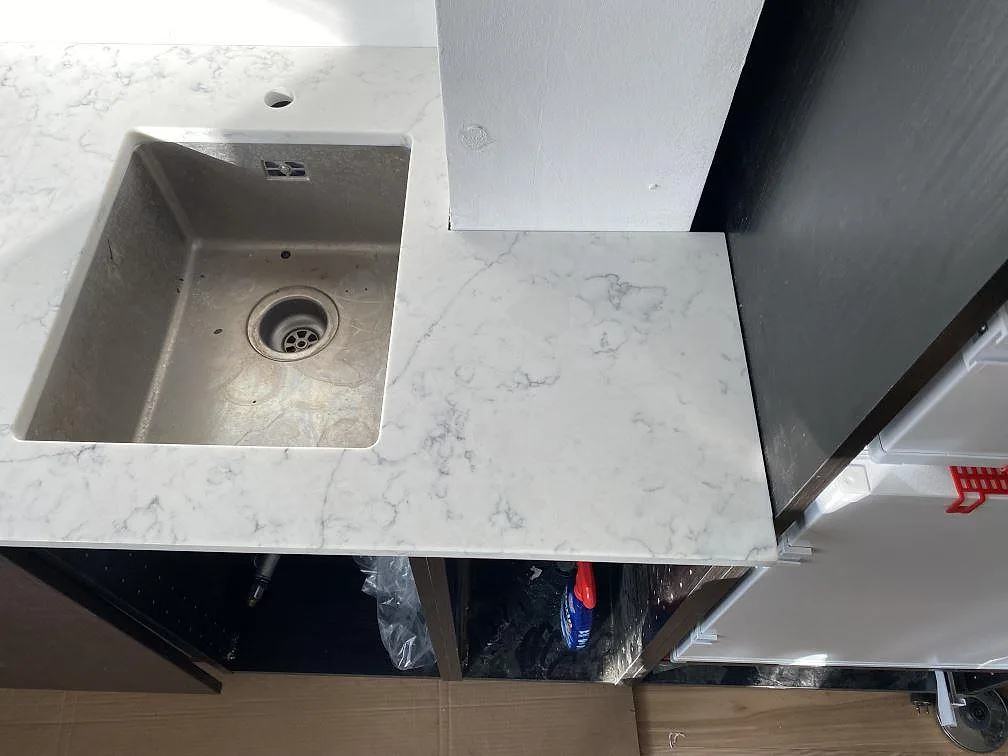 Köksbänkskiva i polerad Technistone Mystery White komposit med diskho och sidoyta under montering i Kbh k.