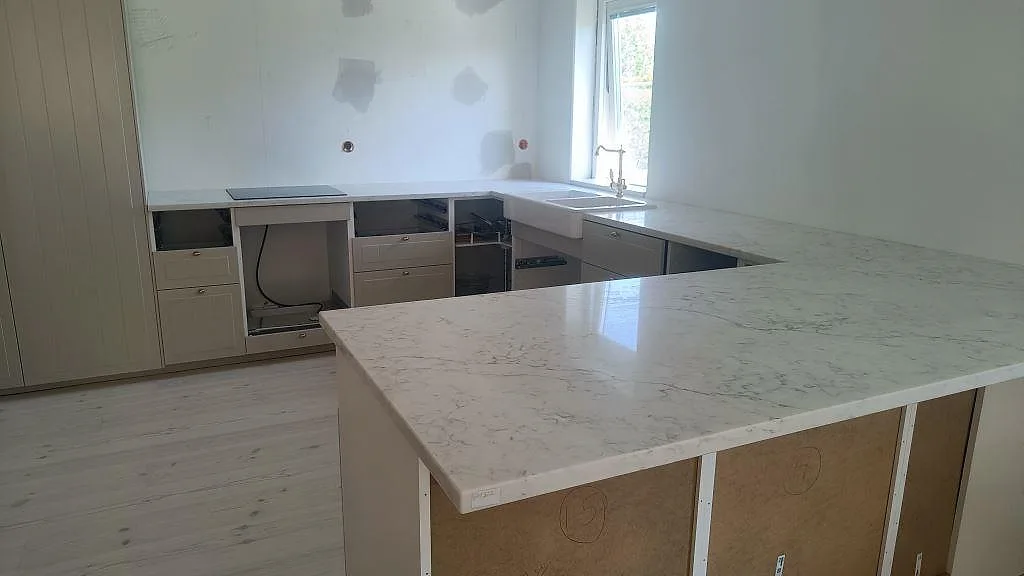 Polerad köksbänkskiva i Technistone Mystery White med halvö, häll och dubbel keramisk diskho i ett kök i Klagshamn.