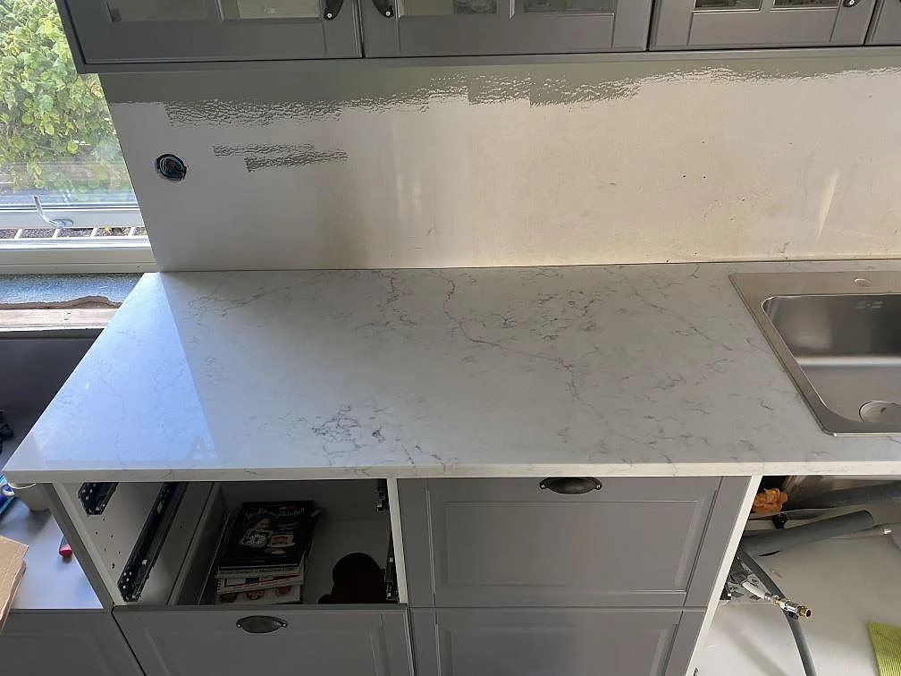 Hörnparti av köksbänkskiva i Technistone Mystery White med förberedd urtagning och stänkskydd i samma vita sten i Klagstorp.