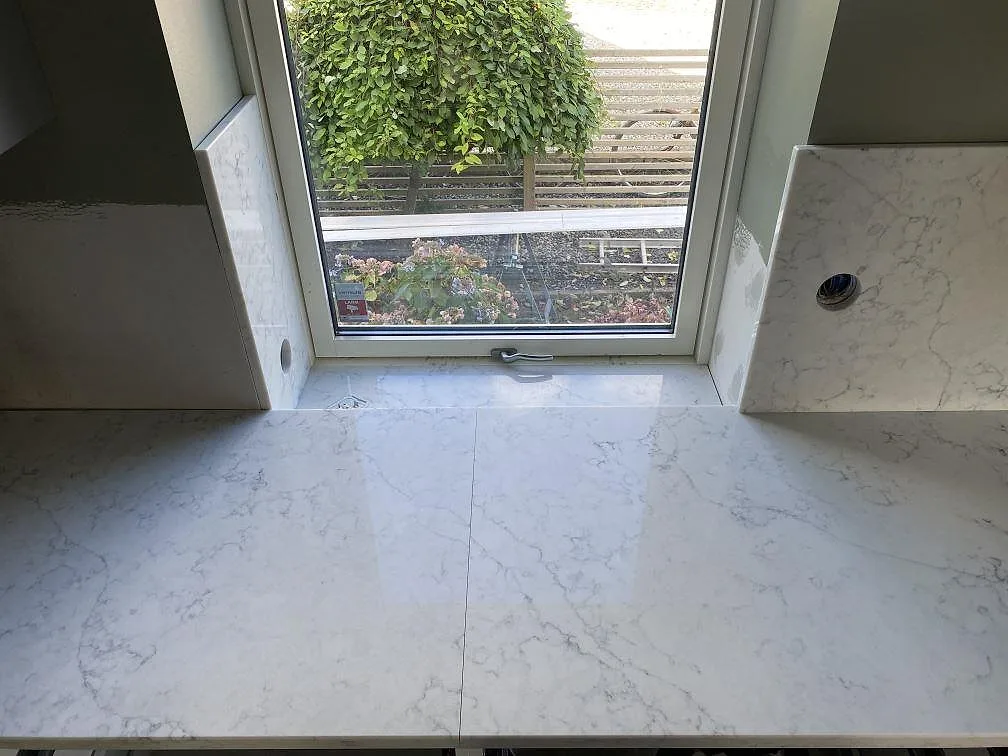 Köksbänkskiva i Technistone Mystery White med fönsterbänk och stänkskydd i samma vita sten i ett kök i Klagstorp.