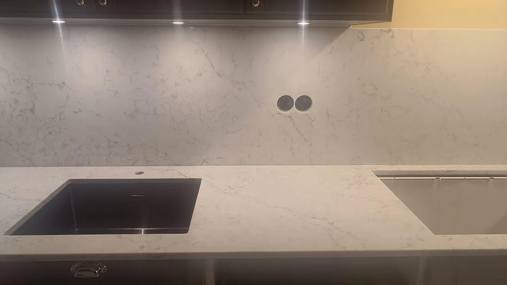 Köksbänkskiva i Technistone Mystery White med två underlimmade diskhoar, en svart komposithoar och en i rostfritt, polerad yta i ett kök i Kristianstad.