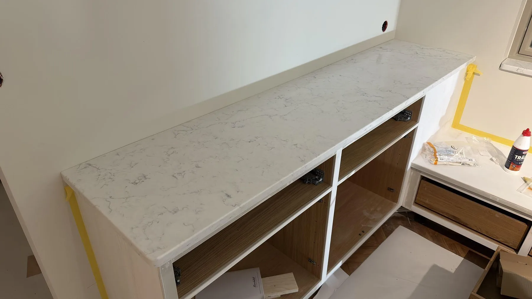 Rak bänkskiva i polerad Technistone Mystery White, vit kvartskomposit, på öppna köksstommar vid fönster i Lidingö.