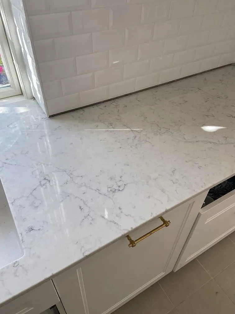 Polerad köksbänkskiva i vit Technistone Mystery White med grå ådring mot vitt metrokakel och mässingshandtag i ett kök i Limhamn.