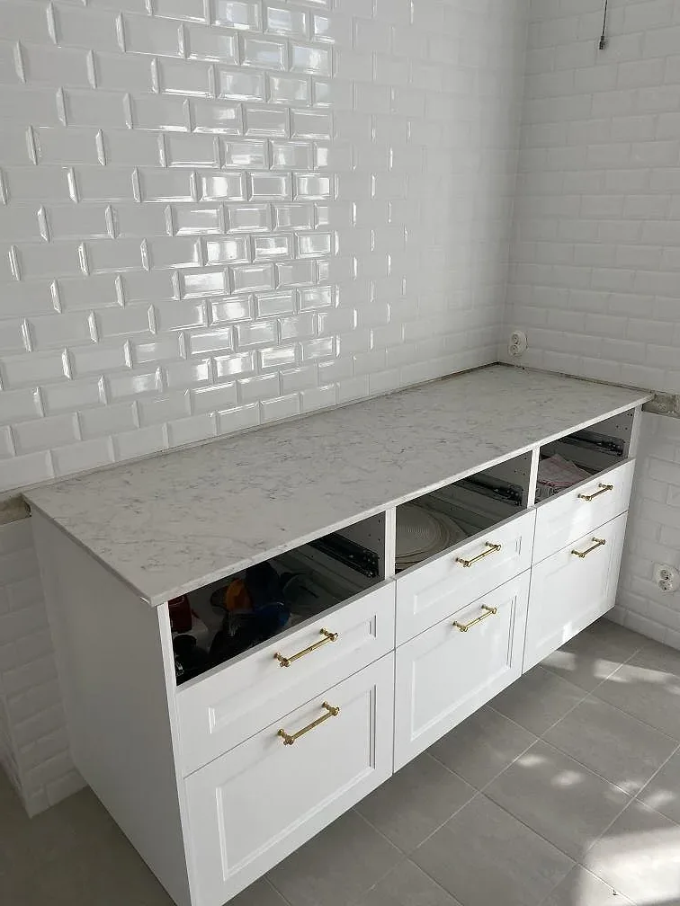Köksrad i Limhamn med polerad bänkskiva i vit Technistone Mystery White, vita ramluckor och mässingshandtag under montering.