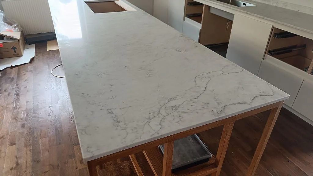 Närbild på polerad köksö i Technistone Mystery White med ljus grund och grå ådring under montering i Limhamn.