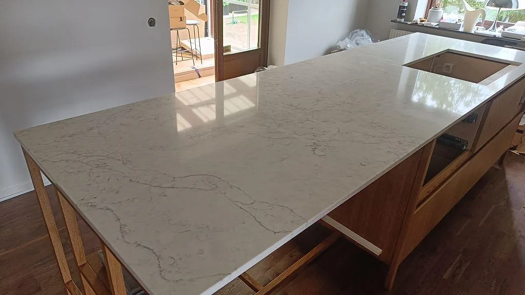 Stor köksö i Technistone Mystery White, polerad komposit, med öppet urtag och trästommar i ett kök i Limhamn.