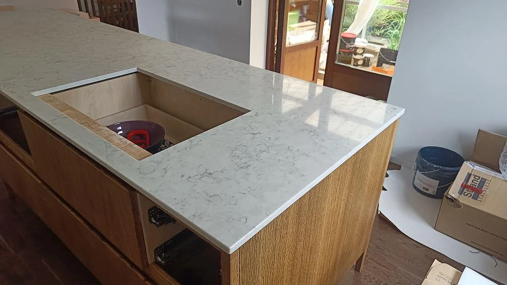 Köksö i Technistone Mystery White, polerad kvartskomposit, med öppet urtag, träinredning och monteringsmaterial i Limhamn.