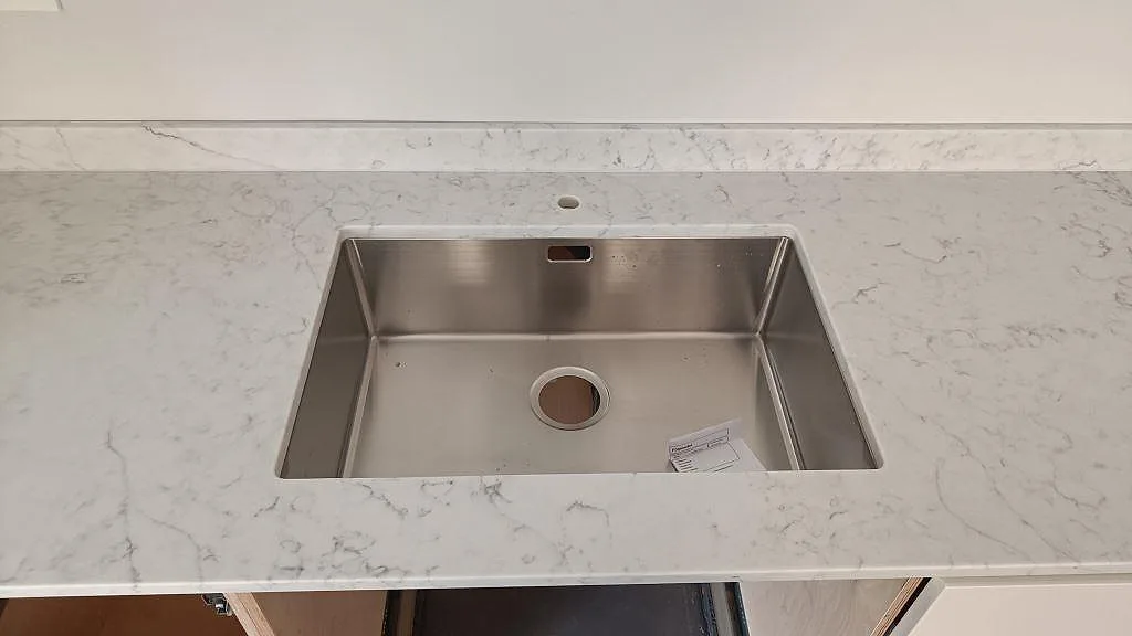 Väggbänk i Technistone Mystery White, polerad komposit, med låg stänkkant och synlig diskho i köket i Limhamn.