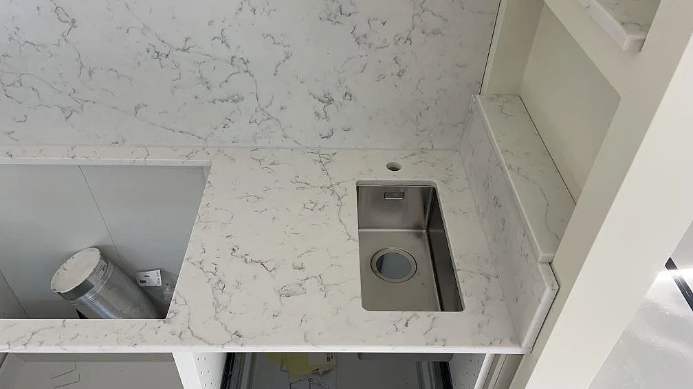 Detalj av polerad Technistone Mystery White med hällöppning, rostfri diskho och stänkskydd vid hylla i Lomma.