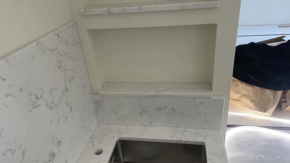 Hörn vid diskhon med polerad Technistone Mystery White, matchande stänkskydd och stenklätt hyllplan i Lomma.