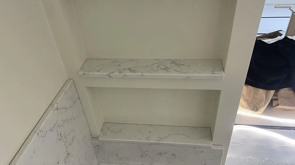 Stenklädda hyllplan i polerad Technistone Mystery White ovanför bänkskiva och stänkskydd i köket i Lomma.