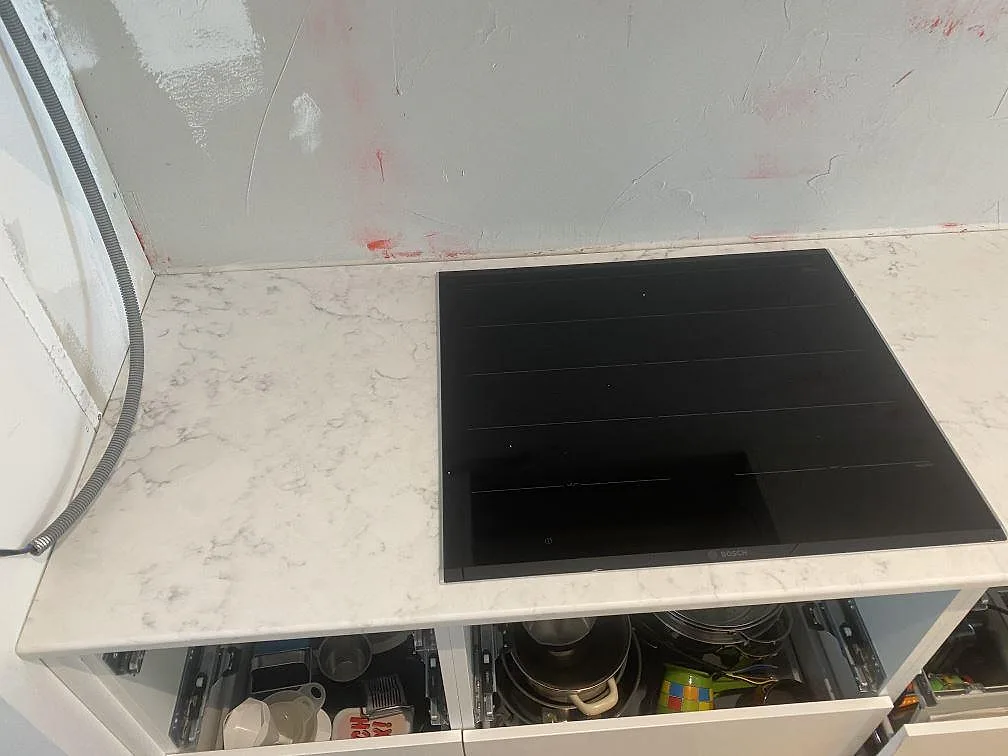 Infälld svart Bosch-induktionshäll i vit polerad köksbänk av Technistone Mystery White kvartskomposit i ett kök i Lund.