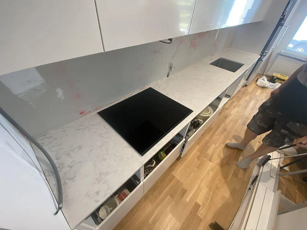 Lång köksbänk i vit Technistone Mystery White komposit med infälld Bosch-induktionshäll och rostfri diskho, fotograferad under montering i Lund.