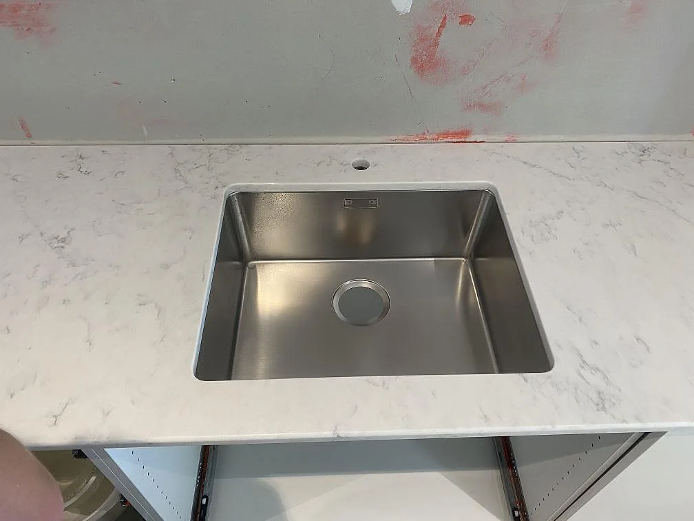 Underlimmad rostfri diskho med separat blandarhål i en polerad köksbänkskiva av Technistone Mystery White komposit i ett kök i Lund.