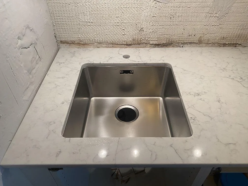 Närbild på underlimmad rostfri diskho i en polerad köksbänkskiva av Technistone Mystery White i Lund.