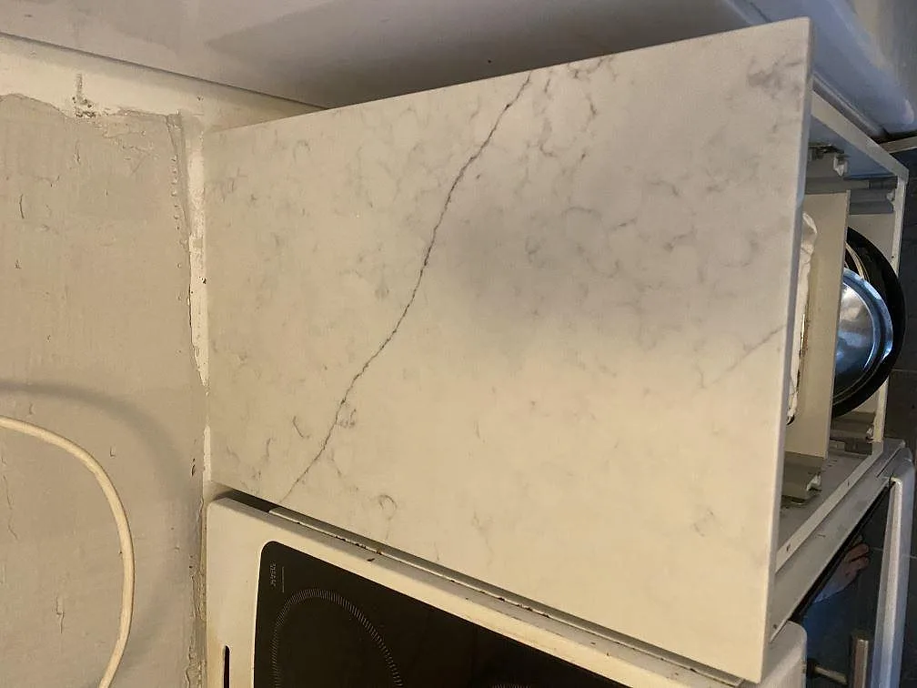Installerad köksbänkskiva i Technistone Mystery White med synlig grå ådring monterad ovanför induktionshäll i ett kök i Lund.