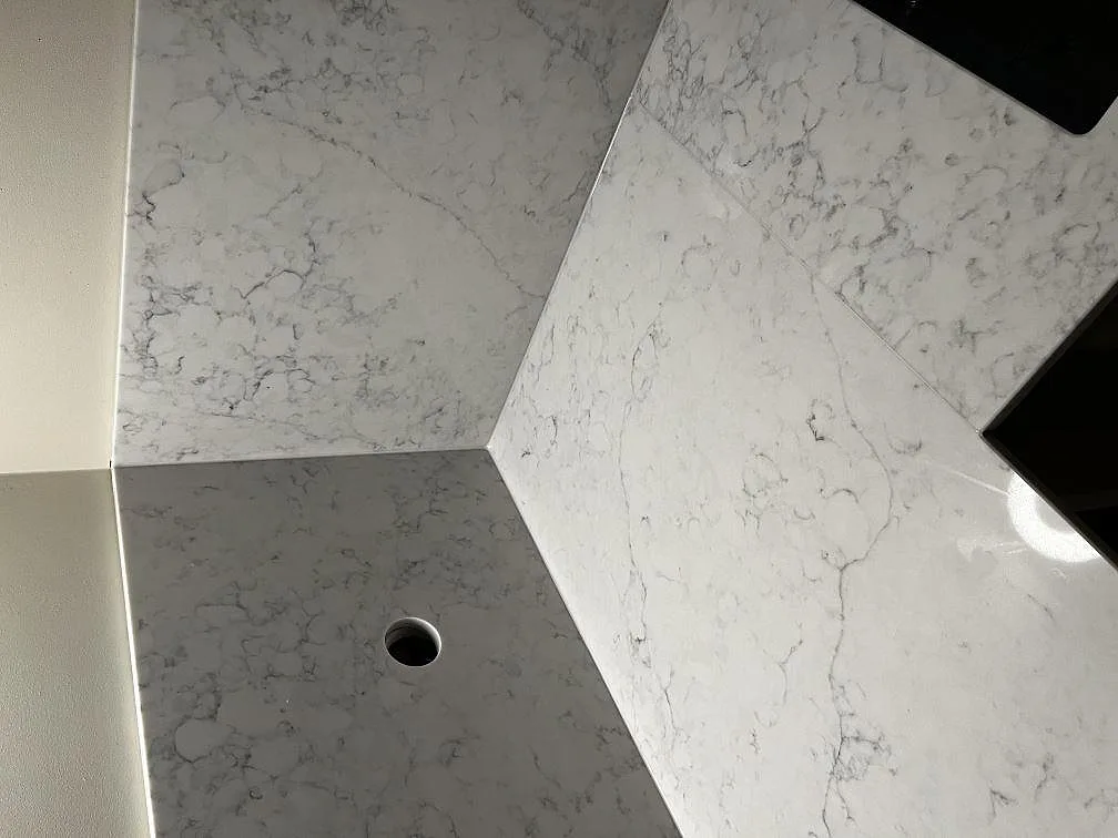 Detalj av polerad Technistone Mystery White komposit med stänkskydd, bänkskiva och genomföring i köket i Malmö.