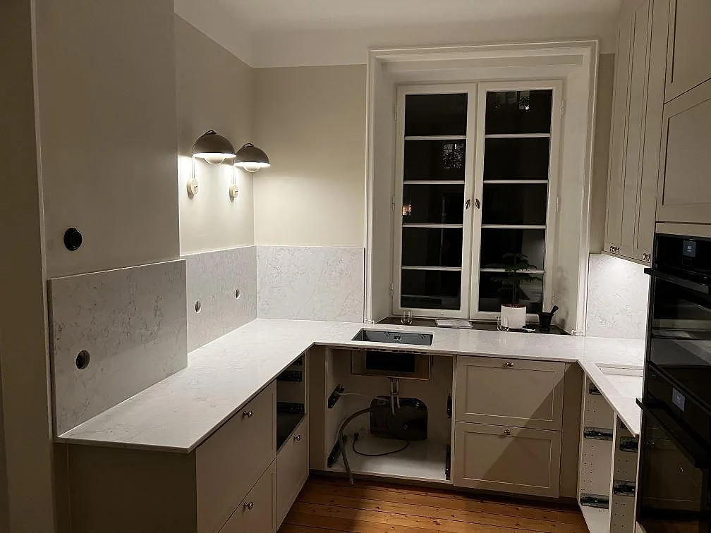 Köksbänkskiva i vit Technistone Mystery White, polerad komposit, med stänkskydd och svart underlimmad diskho i ett U-format kök i Malmö.