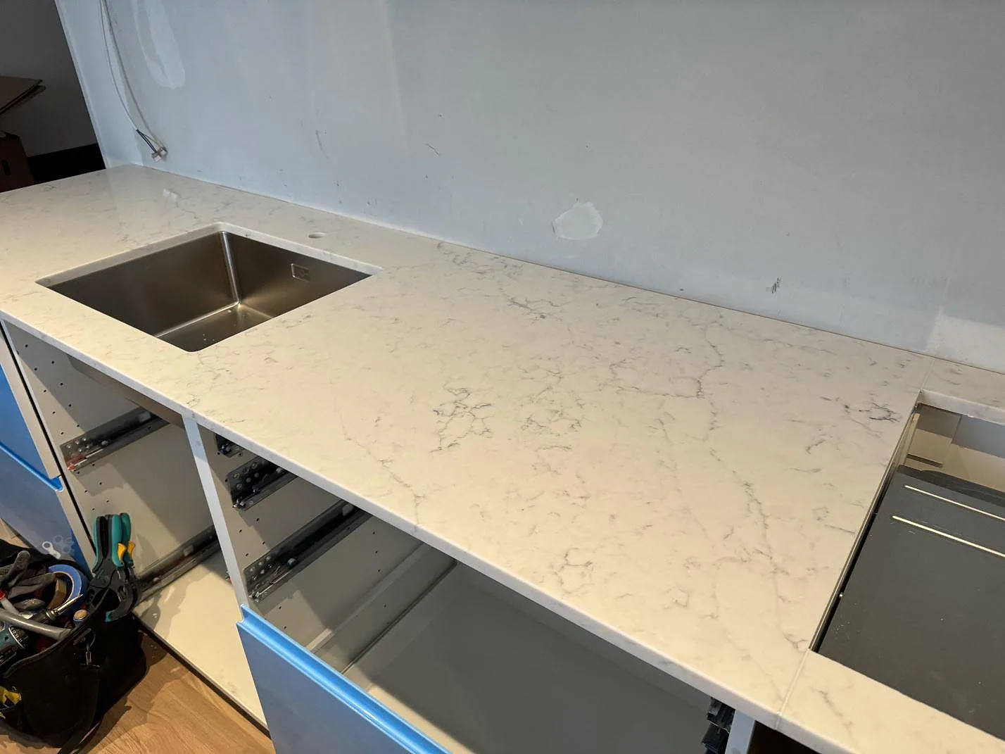 Köksbänkskiva i Technistone Mystery White med underlimmad rostfri diskho, hällöppning och blå köksstommar under montering i Malmö.