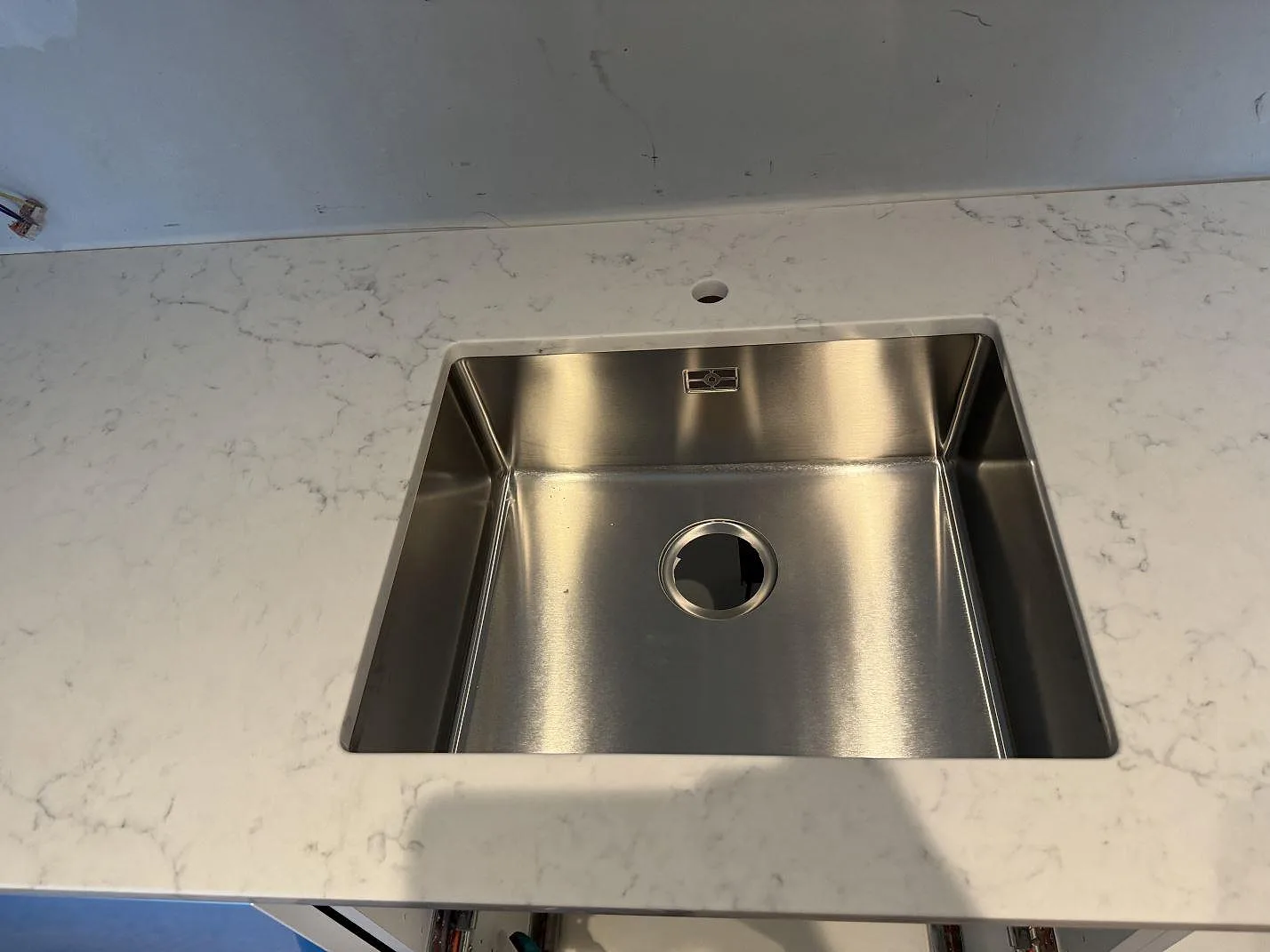 Detalj av underlimmad rostfri diskho i polerad Technistone Mystery White med blandarhål och ljusgrå ådring i Malmö.