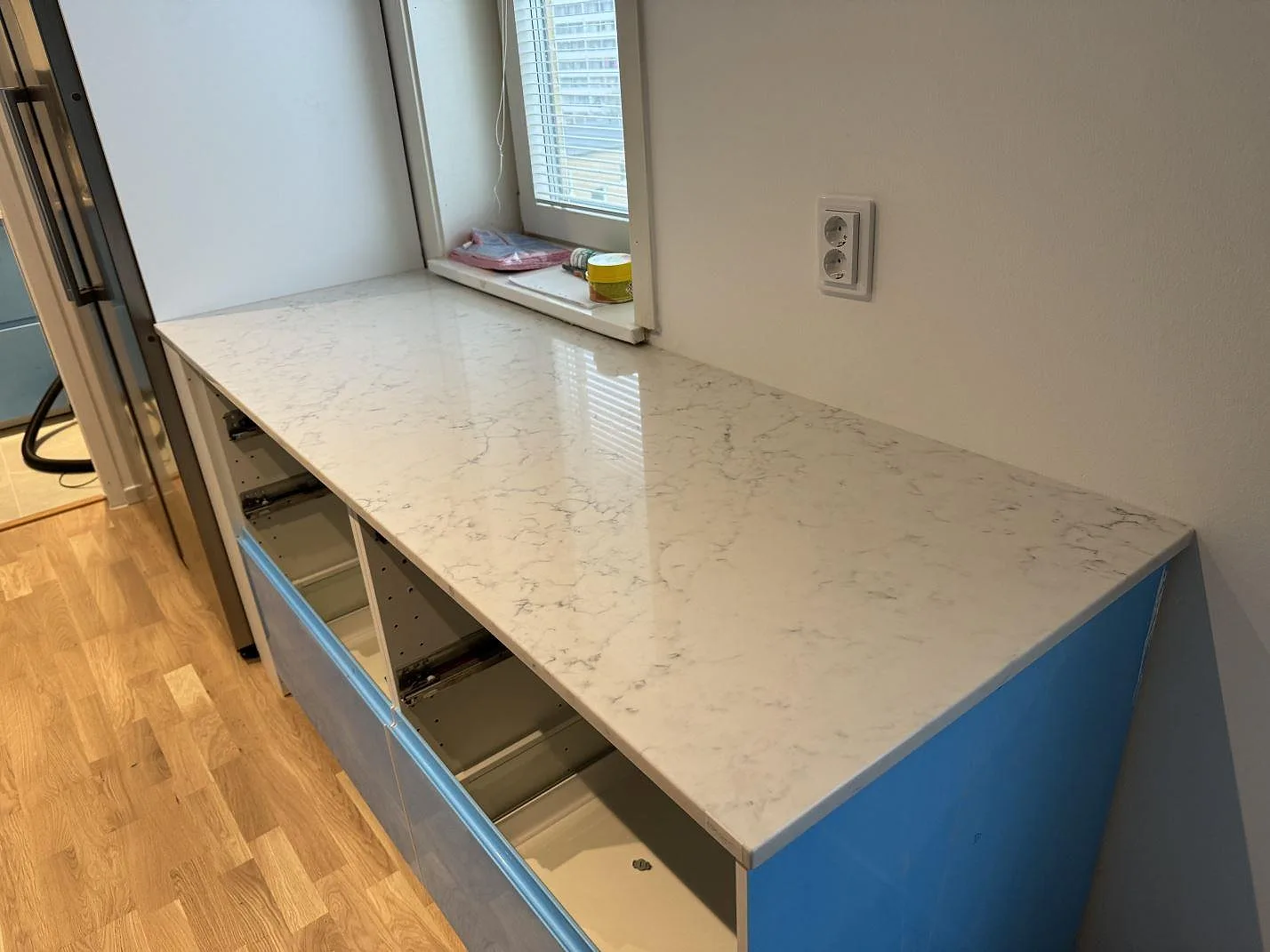 Polerad Technistone Mystery White som bänkskiva vid fönster och blå köksstommar i ett pågående köksmontage i Malmö.