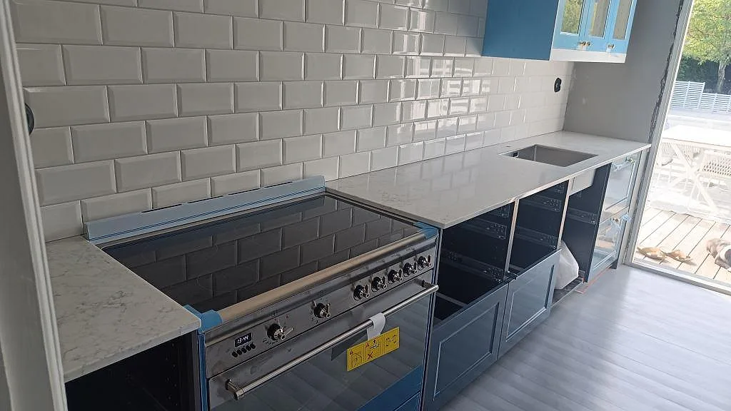 Köksbänkskiva i Technistone Mystery White, polerad kvartskomposit, med fristående spis, mörka stommar och vitt kakel i Malmö.
