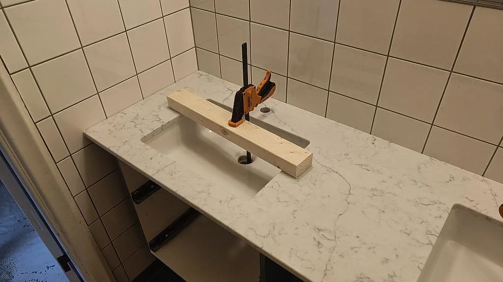 Närbild på polerad Technistone Mystery White-bänkskiva i badrum, med tvättställsöppning, blandarhål och grå ådring i Malmö.