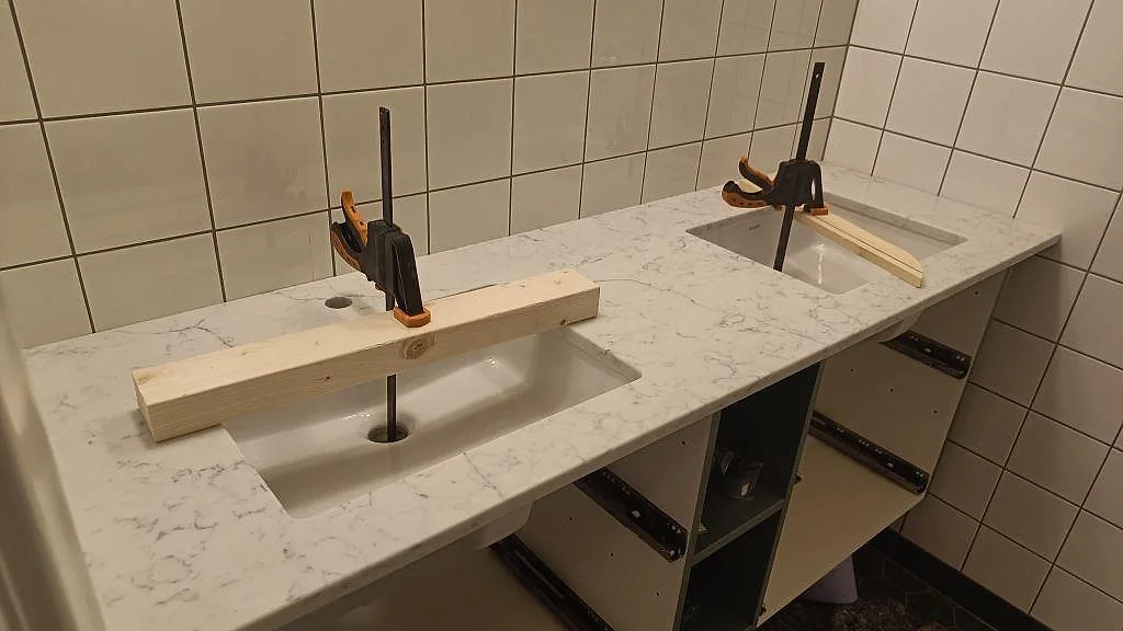 Lång badrumsbänkskiva i polerad Technistone Mystery White komposit med två tvättställ och öppna stommar i Malmö.