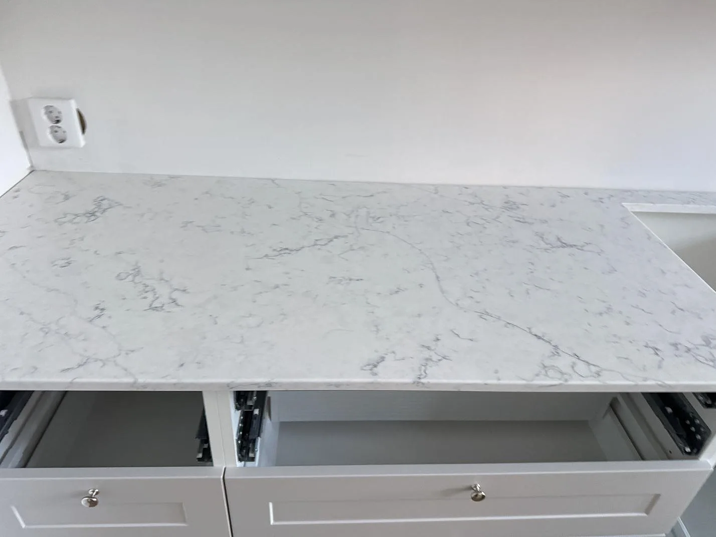 Lång köksbänkskiva i polerad Technistone Mystery White, vit kvartskomposit med diskret ådring, på öppna köksstommar i Malmö.