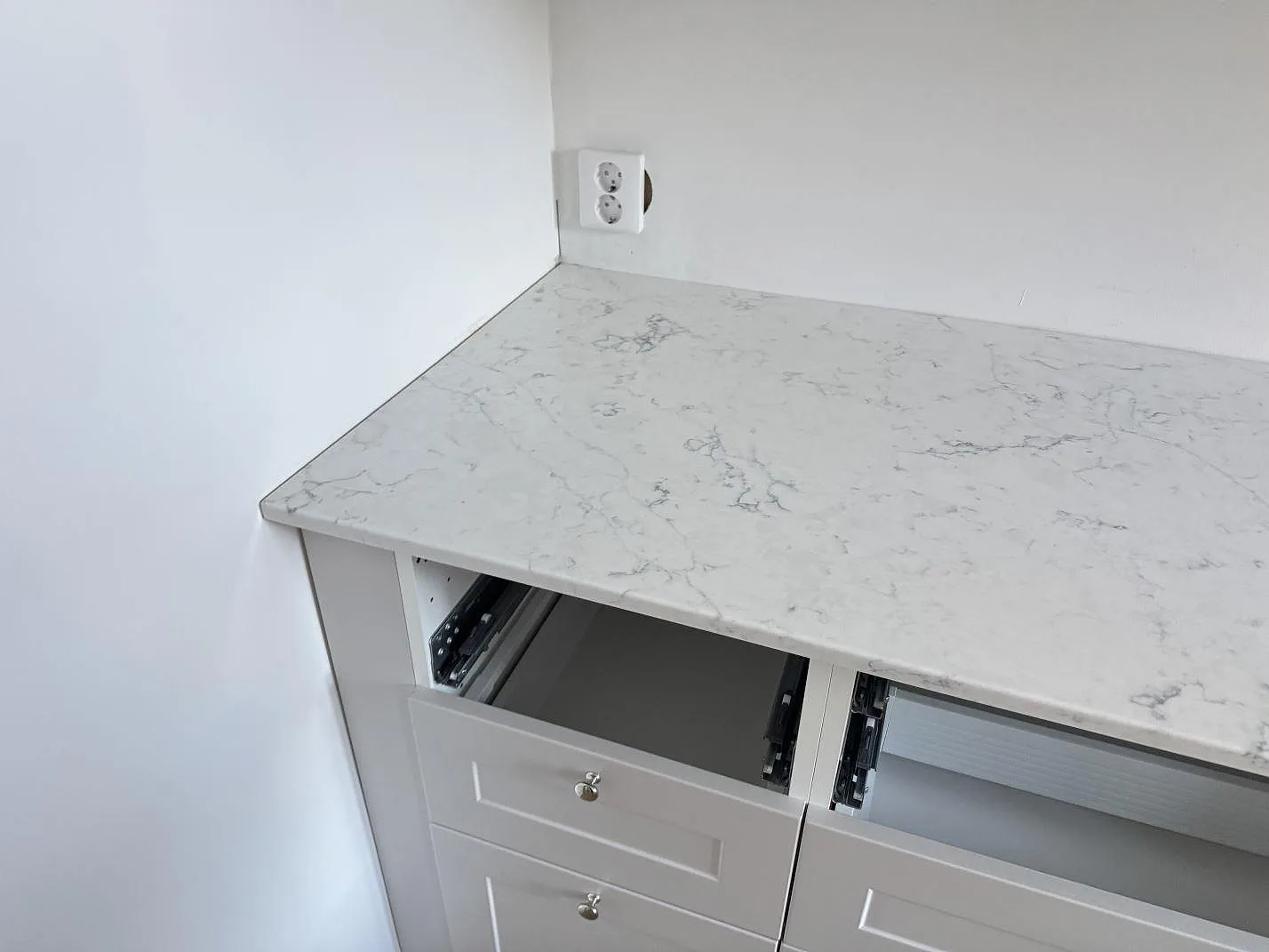Vänster del av köksbänkskiva i polerad Technistone Mystery White med grå ådring, öppna lådor och vägguttag i Malmö.