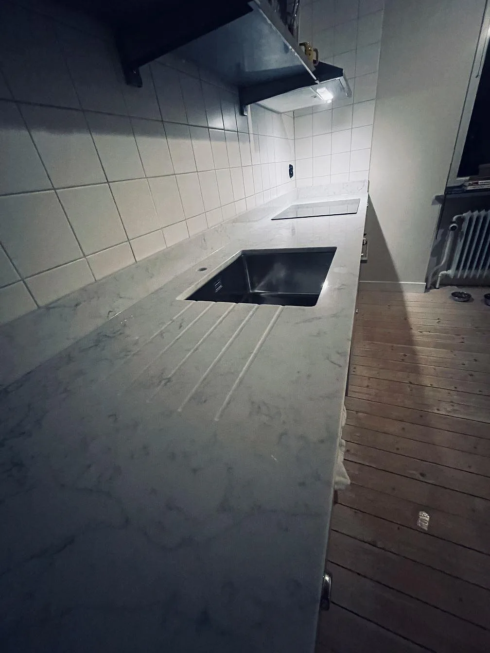 Polerad bänkskiva i Technistone Mystery White med underlimmad rostfri diskho och frästa avrinningsspår längs den raka köksbänken i Malmö.