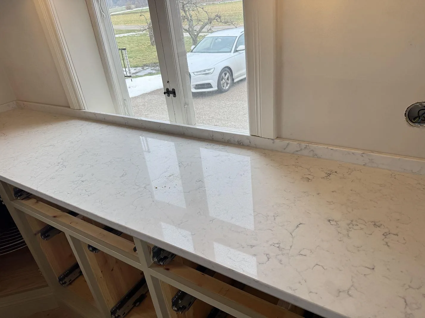 Polerad köksbänkskiva i Technistone Mystery White med spegelblanka reflektioner och grå ådring mot ett fönster i ett kök i Näsum.