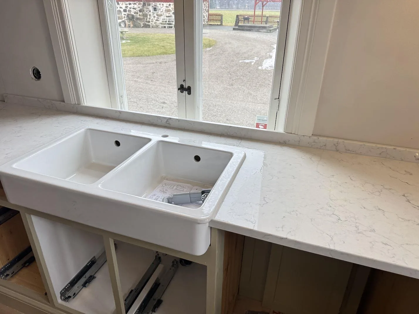 Vit dubbel keramikho med förhöjd framkant nedsänkt i polerad Technistone Mystery White köksbänkskiva framför ett fönster i ett kök i Näsum.