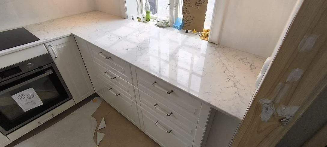 Närbild av blank Technistone Mystery White bänkskiva med ljus botten och grå ådring i ett kök under montering i Norrtälje Rö.