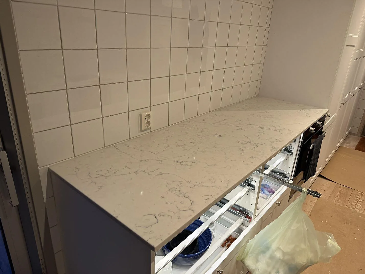 Lång köksbänk i polerad Technistone Mystery White komposit mot vitt kakel och vit köksinredning under montering i Nyehusen.
