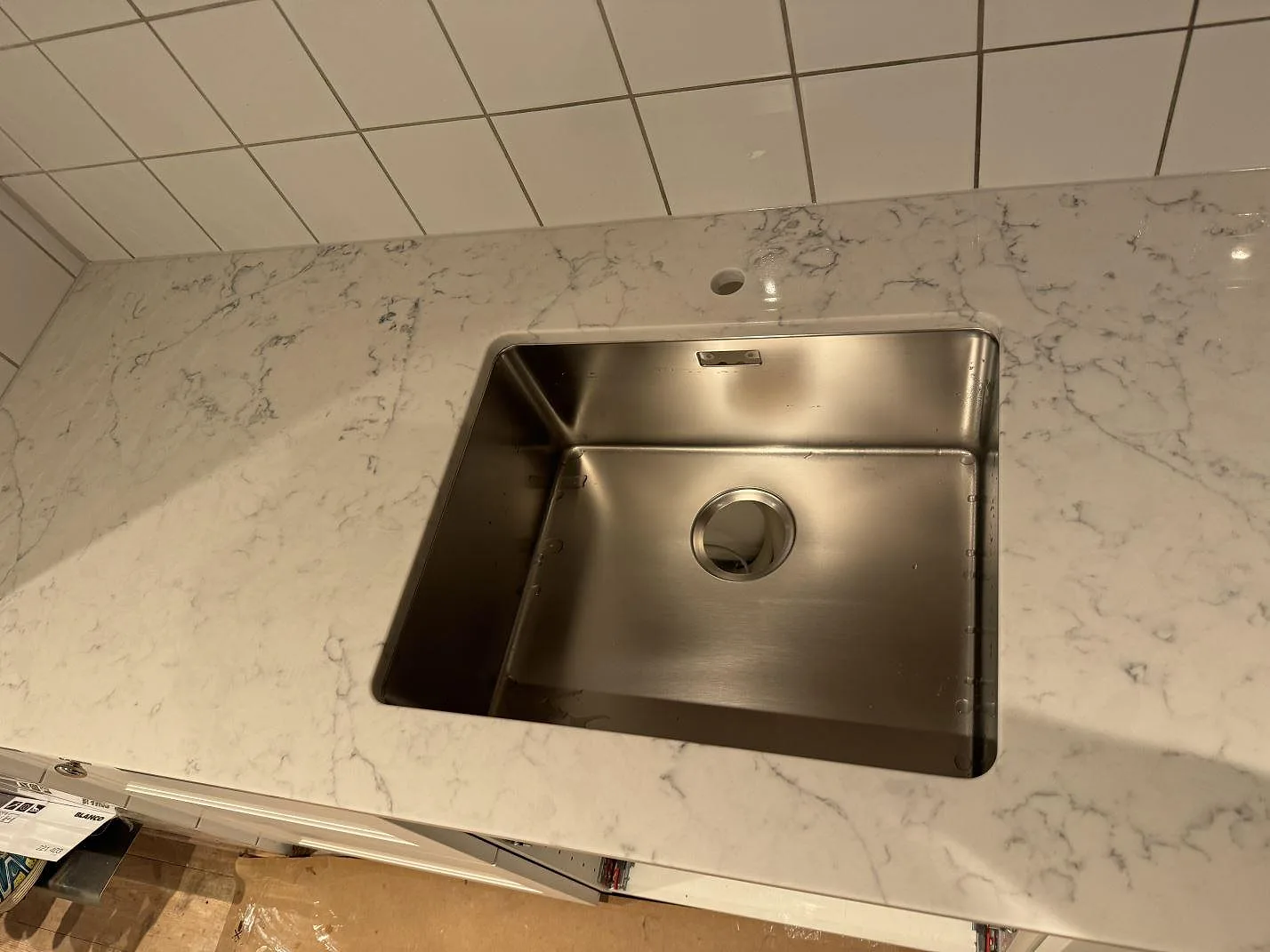 Detalj av polerad Technistone Mystery White bänkskiva med underlimmad rostfri diskho och borrhål för blandare i Nyehusen.