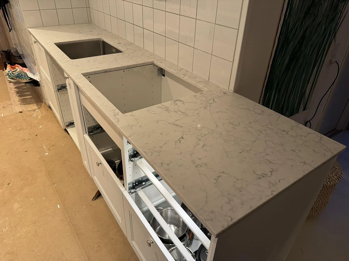 Polerad köksbänkskiva i Technistone Mystery White med grå ådring, rostfri diskho och förberedd hällöppning i ett kök i Nyehusen.
