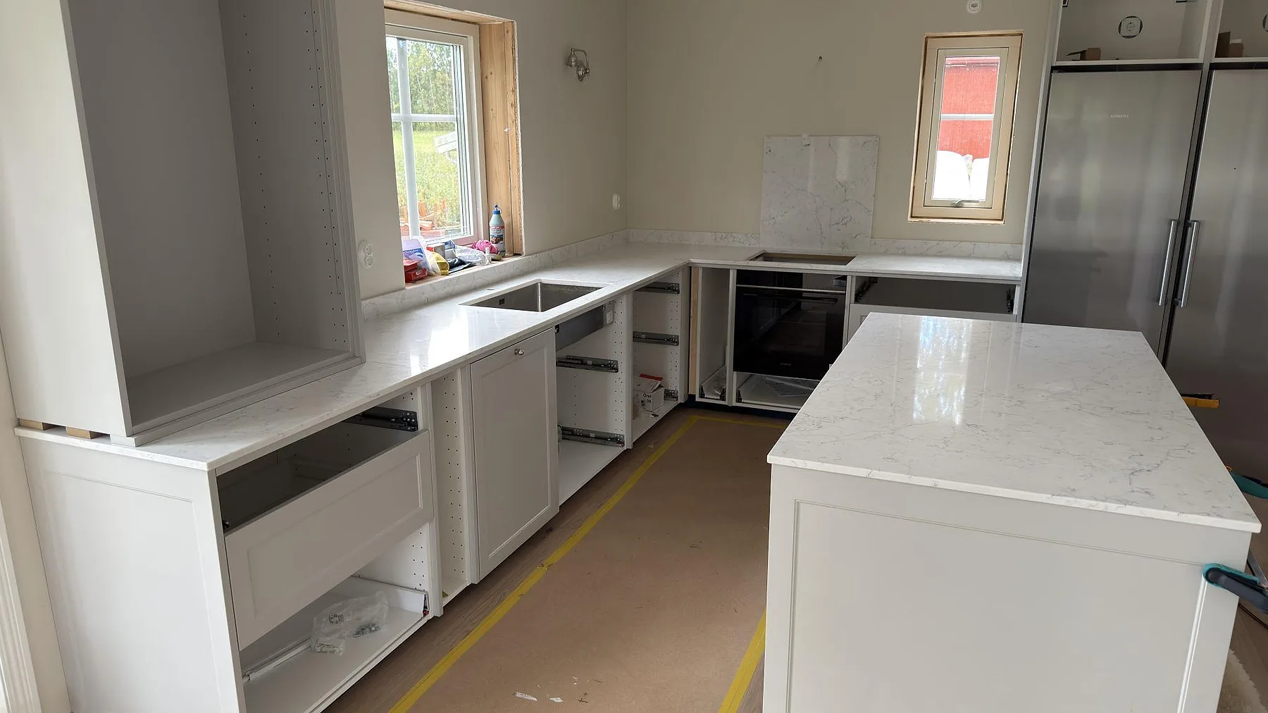 Polerad köksbänkskiva i Technistone Mystery White med köksö, diskhozon och hällöppning under montering i Örebro.